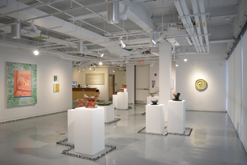 View into the central gallery at Dowd Gallery featuring sculptural objects produced by Jeremiah Donovan, professor of ceramics, Jillian McEvoy, instructor of ceramics, paintings by Stephen Alexander Clark, processor of painting, and floor installation by Bryan Valentine Thomas, instructor of design and drawing, at the Art and Art History Department.  