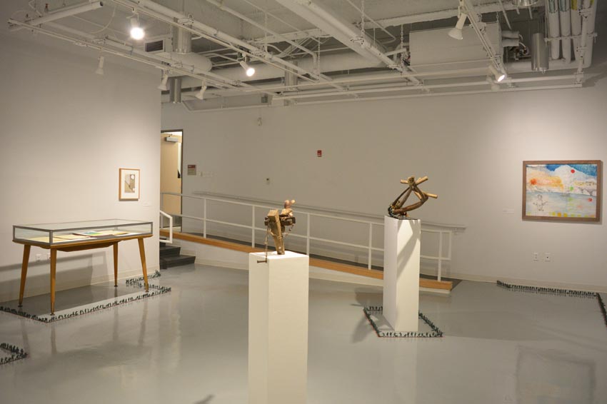 View into the west gallery at Dowd Gallery featuring sculptures produced by Scott Oldfield, instructor of drawing, and prints by Charles Heasley, professor of printmaking and other courses, and floor installation by Bryan Valentine Thomas, instructor of design and drawing, at the Art and Art History Department. 