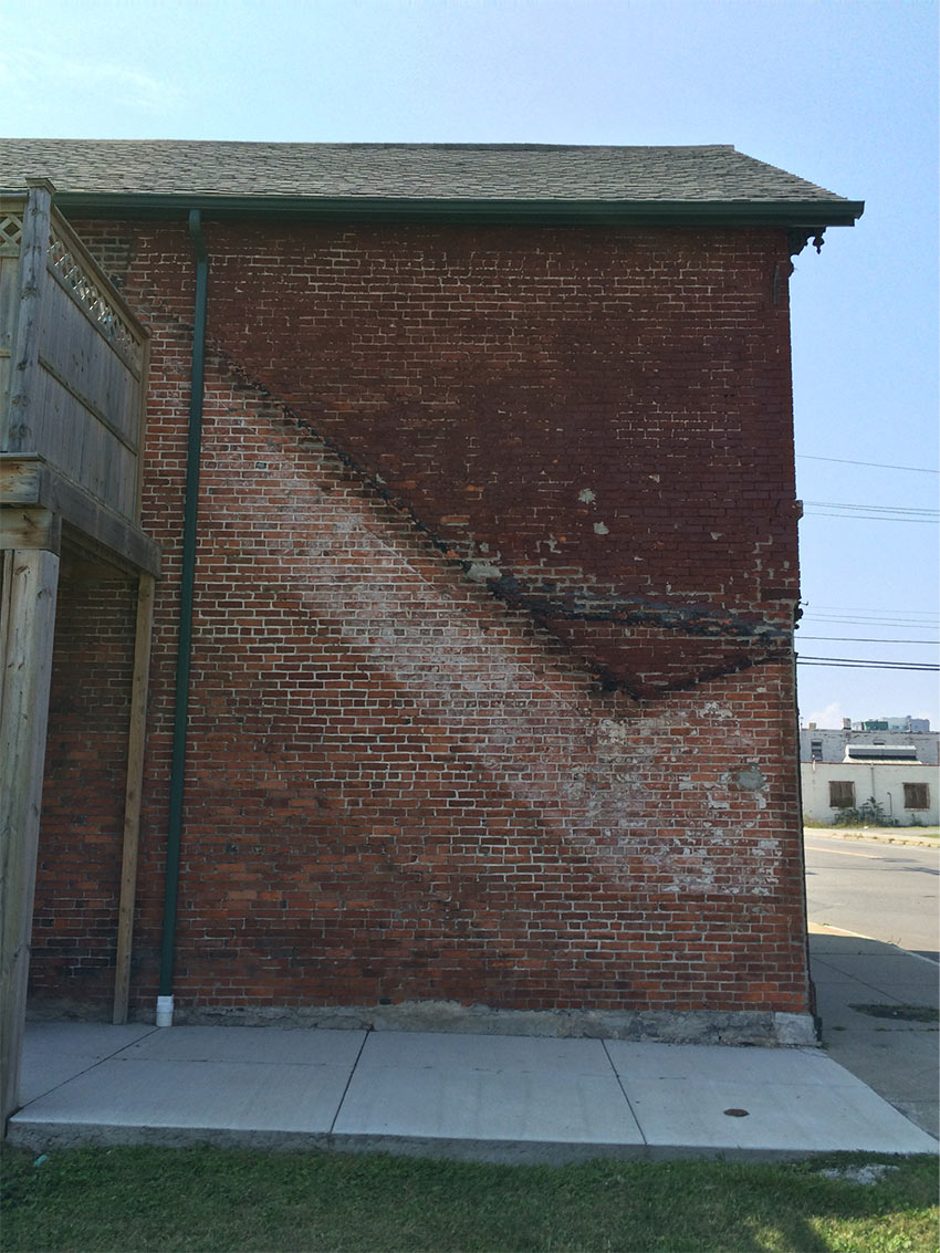 A brick building facade showing wear from a fire escape that was apparently removed.