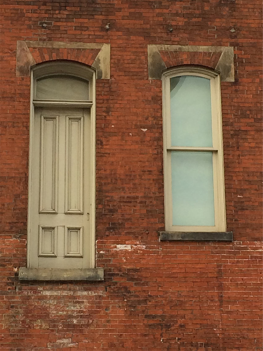 A brick wall with a window and an inaccessible door above ground level