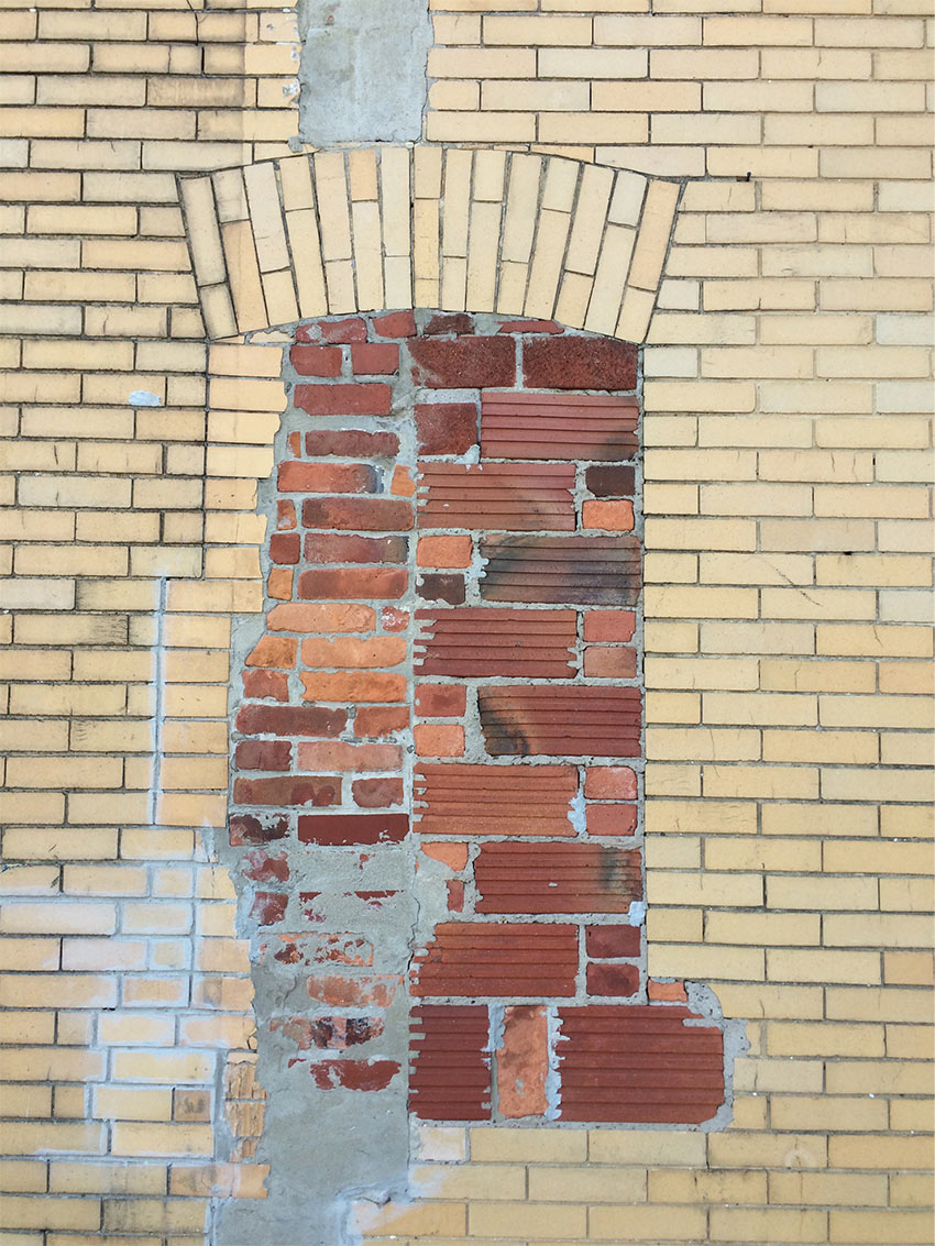 Close-up of a yellow brick building with new brock mortared into what was previously a window