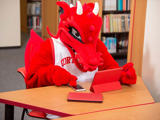 Blaze the Red Dragon mascot in the library, using several mobile devices