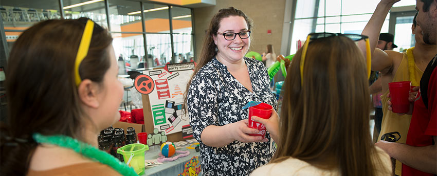 Whilte tabling for healthy spring break, a graduate assitant hands out cups with decorative drink umbrellas to students in the Student Life Center
