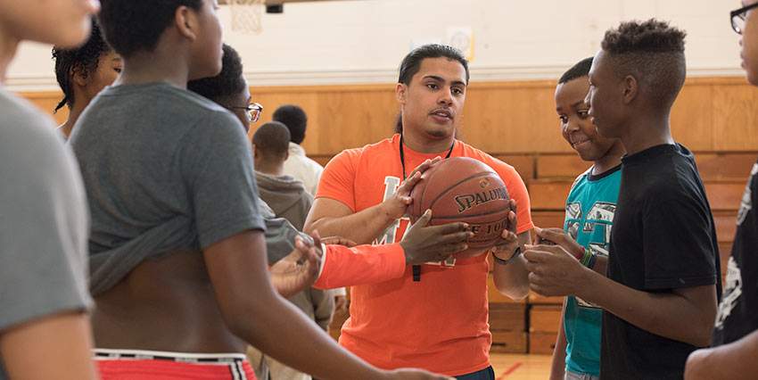 A C.U.R.E. alumni coaches a group of high school students on a basketball court